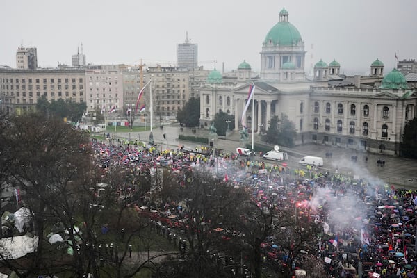 Protesters light flares as the march past the Parliament building during a major rally against populist President Aleksandar Vucic and his government, in downtown Belgrade, Serbia, Saturday, March 15, 2025. (AP Photo/Darko Vojinovic)