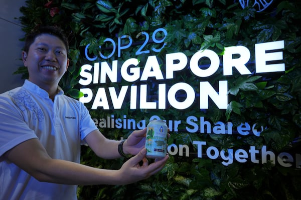 Nick Chow, part of the COP29 Singapore Pavilion team, poses for a photo with NewBrew, beer made with treated wastewater, during the COP29 U.N. Climate Summit, Friday, Nov. 15, 2024, in Baku, Azerbaijan. (AP Photo/Peter Dejong)