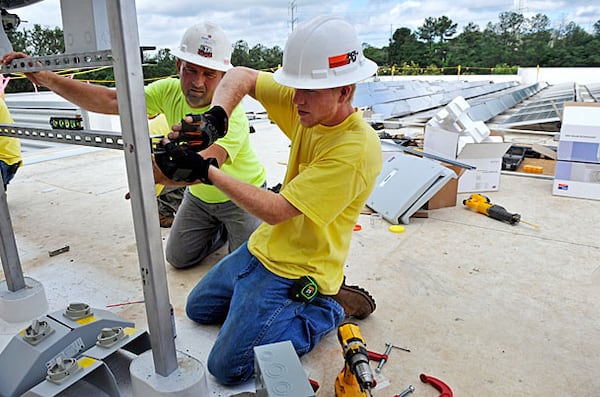 Robert Pike (left) and Jason Wrinkle with First Century Energy mount inverters and electrical disconnects for the solar array at McKenney's headquarters in Atlanta. Georgia has been a big beneficiary of green incentives. Will its growth in areas such as the manufacturing of electric vehicles continue if Donald Trump rolls back those initiatives at the federal level? Courtesy of Bita Honarvar.