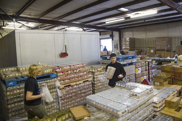 Sweetwater Mission volunteers Katie Mason (left) and Anderson Villamizar (right) prepare canned food items for pickup during the food distribution “drive-through.” ALYSSA POINTER/ALYSSA.POINTER@AJC.COM