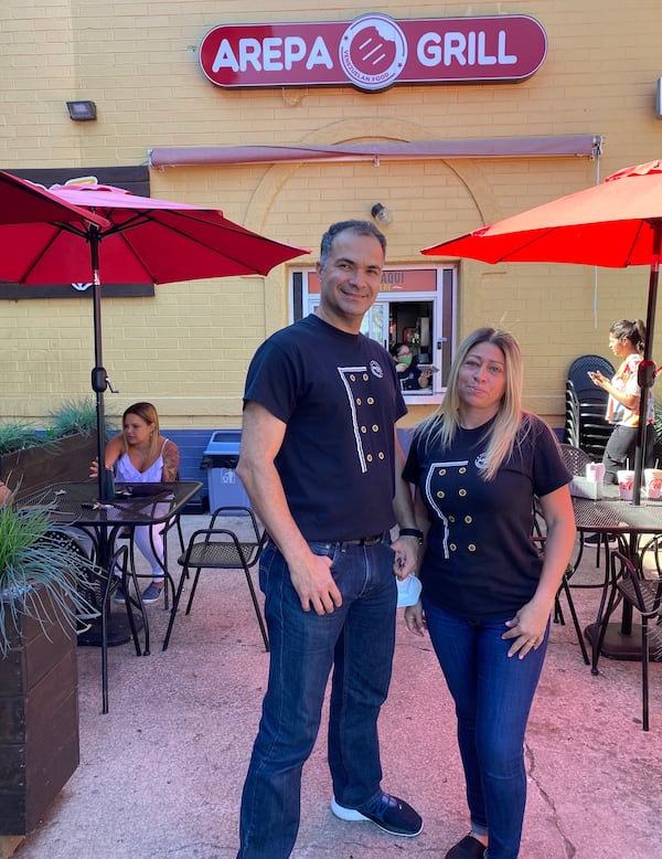 Married Arepa Grill owners Pedro and Claudia Cardenas stand on the patio of their restaurant inside Plaza Fiesta. Ligaya Figueras/ligaya.figueras@ajc.com
