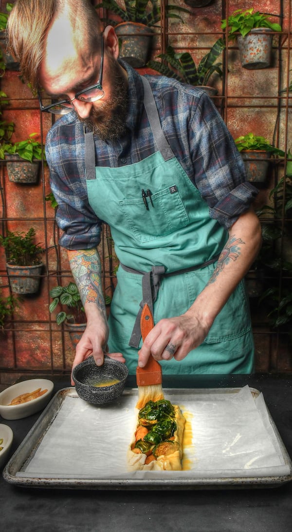 Two Urban Licks executive chef Shain Wancio adds an egg wash to the exterior of the assembled oven components inside the puff pastry of a savory galette. Garnishes will be added later. (Styling by chef Shain Wancio / Chris Hunt for the AJC)