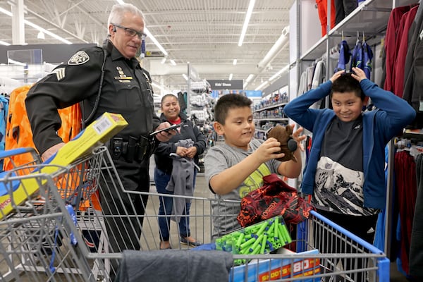 Sergeant Carlos Rubio, left, watches as Danny Ramirez, 8, center, looks over his toys at Walmart, Tuesday, December 13, 2022, in Canton, Ga. Also pictured is Danny’s older brother Christopher Ramirez, 10, right, and mother Bonifacia Argueta, second from left. The children were shopping with the Cherokee County Deputies during their annual ‘Shot with a cop’ event to buy toys for underprivileged children. (Jason Getz / Jason.Getz@ajc.com)