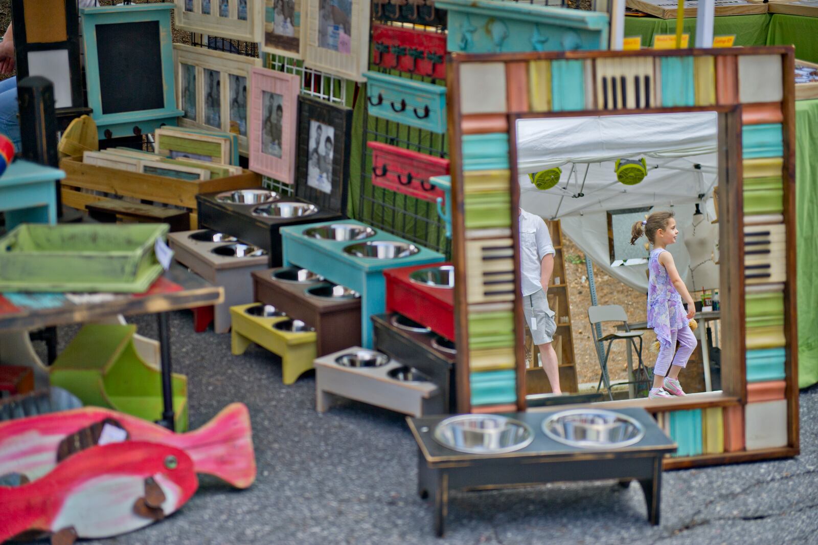 Tayla Berzack (right) is reflected in a mirror as she passes by Suzanne and Don Puckett's booth during the Sandy Springs Artsapalooza on Sunday, April 13, 2014. The third annual festival featured 150 painters, photographers, sculptors, leather and metal craft persons, glass blowers, jewelers and more.