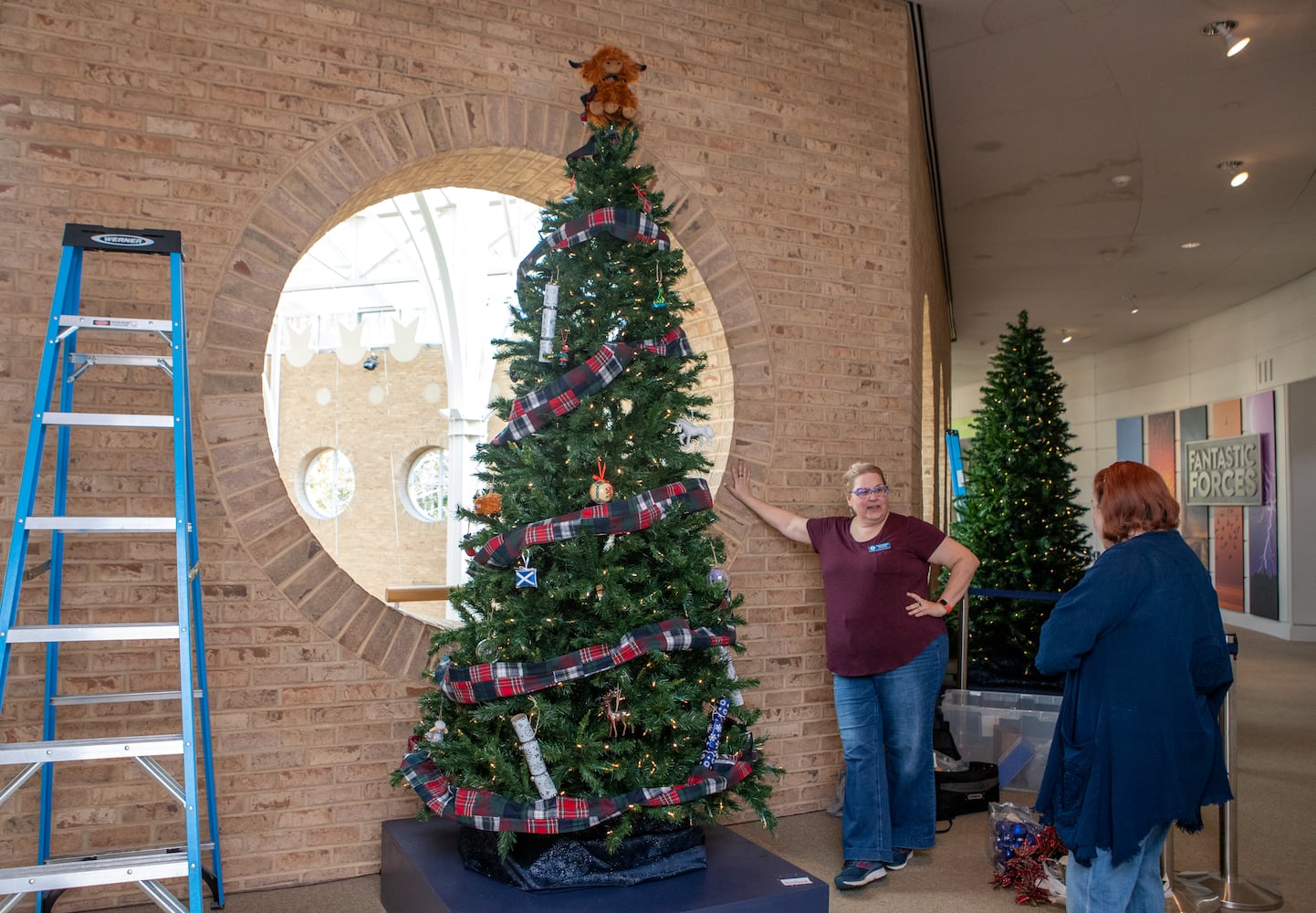 Fernbank Museum prepares for the 15th annual "Winter Wonderland" exhibit where Atlanta cultural partners, including President of St. Andrews Society Catherine Olson, center, and her mother Caren Miears decorate the Scottish tree on Saturday, Nov 16, 2024 . Exhibit opens November 23 and runs through January 12, 2025. (Jenni Girtman for The Atlanta Journal Constitution)