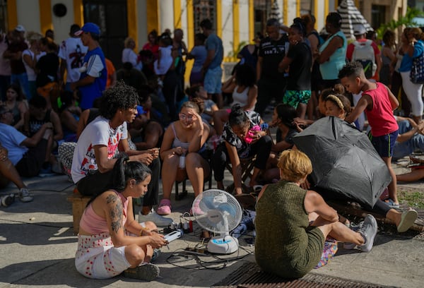 Residents charge their electronic devices on a street during a general blackout in Havana, Saturday, March 15, 2025. (AP Photo/Ramon Espinosa)