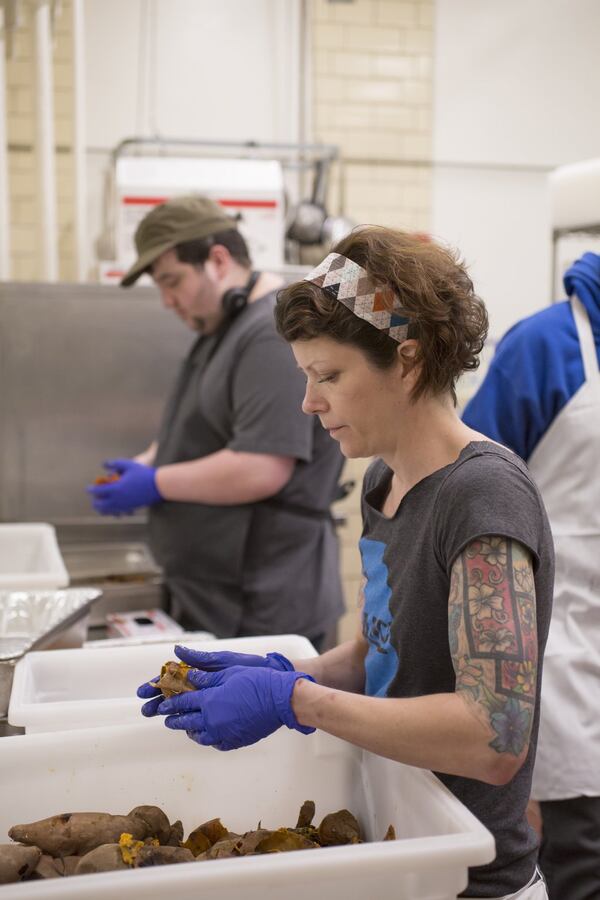 Preparing breakfast and lunch from scratch means hours of prep. Here, Foster Deck (rear) and Lori McKay peel the bushels of roasted sweet potatoes needed for a Southern-style vegetable plate in a school lunch last year. Photo: Kelley Klein