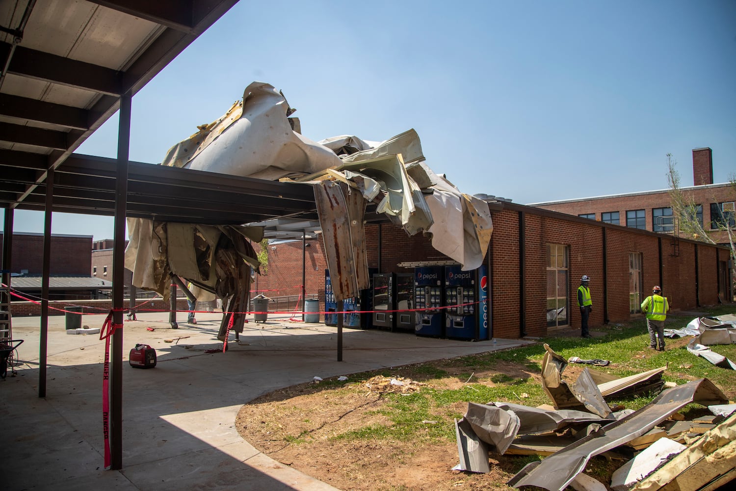 Workmen survey the damage to the outside of Newnan High School. (Alyssa Pointer / Alyssa.Pointer@ajc.com)