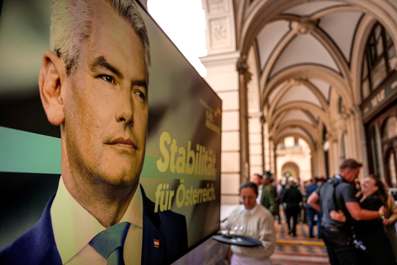 People gather next to a poster of Austrian Chancellor Karl Nehammer at the OVP, Austrian People's Party, headquarters in Vienna, Austria, Sunday, Sept. 29, 2024. (AP Photo/Andreea Alexandru)