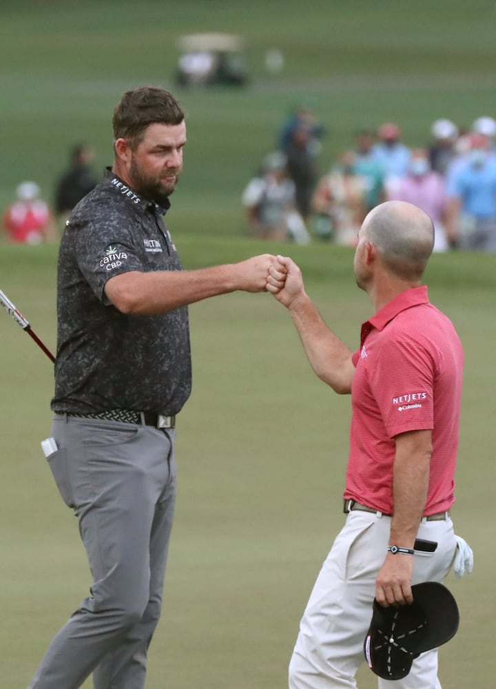 April 10, 2021, Augusta: Marc Leishman and Brian Harman give each other a fist bump as they finish their third round during the Masters at Augusta National Golf Club on Saturday, April 10, 2021, in Augusta. Curtis Compton/ccompton@ajc.com