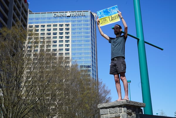 A protester climbs on a column outside Centennial Olympic Park at a rally on Saturday, March 19, 2022 to raise awareness about the plight of children in the war in Ukraine. Some called for the establishment of a no-fly zone over the country.