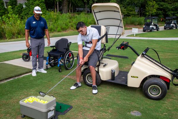 Mak Yost (right) works with Bobby Jones golf pro Orlando Rodriguez using adaptive golf equipment like the Solo Rider that helps him stand and hit the golf ball. PHIL SKINNER FOR THE ATLANTA JOURNAL-CONSTITUTION.