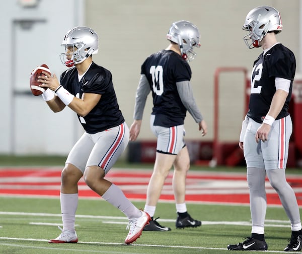 Ohio State quarterback Justin Fields, left, takes a snap in front of teammates quarterback Daniel Vanatsky, center, and quarterback Matthew Baldwin during an NCAA college football practice in Columbus, Ohio, Wednesday, March 6, 2019. (AP Photo/Paul Vernon)