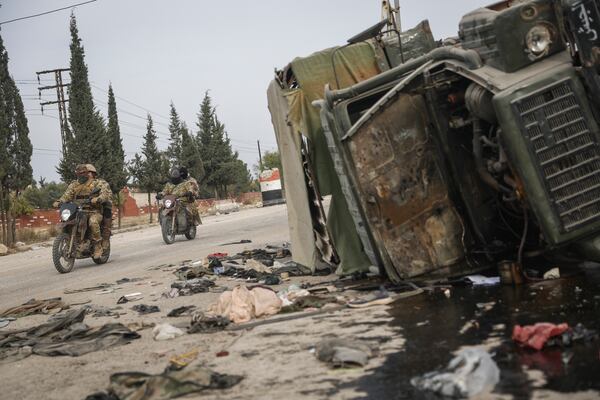 Syrian opposition fighters drive past a damaged government vehicle south of Hama, Syria, on Saturday, Dec. 7, 2024. (AP Photo/Ghaith Alsayed)