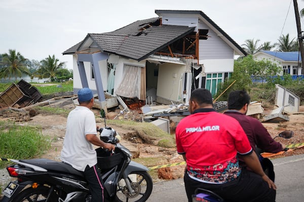 Motorists survey a house damaged by a flood in Tumpat, on the outskirts of Kota Bahru, Malaysia, Tuesday, Dec. 3, 2024. (AP Photo/Vincent Thian)