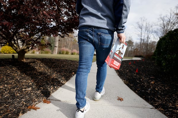 A person who supports Senate hopeful Herschel Walker, a Republican, distributes flyers in Alpharetta ahead of the Dec. 6 runoff election against U.S. Sen. Raphael Warnock. (Miguel Martinez/AJC).