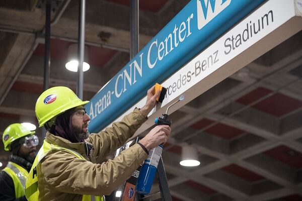 Tim Carl (second from left) of Advantage Graphics & Signs uses a torch to ensure the cohesiveness of the new Mercedes-Benz signage at the  MARTA Dome/GWCC/Philips Arena/CNN Center Transit in Atlanta, Wednesday, Jan. 16, 2019. Advantage Graphics & Signs worked in the transit station on Wednesday to replace signage that mislabeled Atlanta's two newly named sport stadiums. (Alyssa Pointer/Alyssa.Pointer@ajc.com)