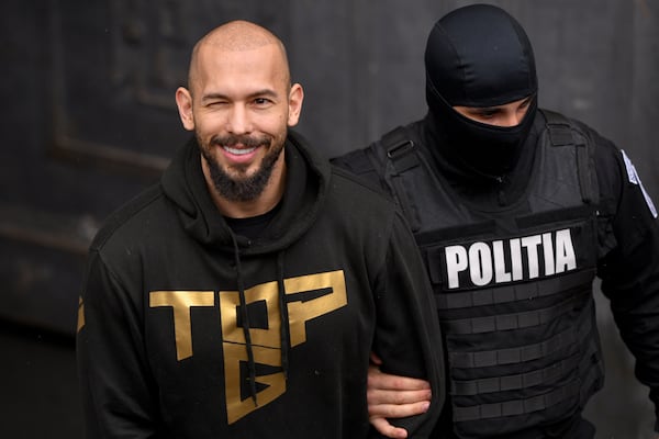 A police officer escorts Andrew Tate, center, handcuffed, from the Court of Appeal in Bucharest, Romania, Tuesday, March 12, 2024. Online influencer Andrew Tate was detained in Romania and handed an arrest warrant issued by British authorities, his spokesperson said Tuesday. (AP Photo/ Alexandru Dobre)