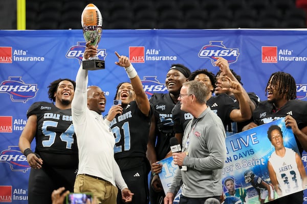 Cedar Grove head coach John Adams celebrates with players as he lifts the trophy celebrating their win against Savannah Christian in the Class 3A GHSA State Championship game at Mercedes-Benz Stadium, Wednesday, December. 13, 2023, in Atlanta. Cedar Grove won 49-28. (Jason Getz / Jason.Getz@ajc.com)