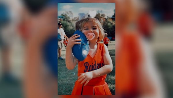 Cate Gruehn holds a football while attending her older brother's football game as a toddler.