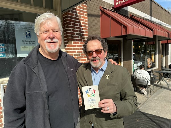 "The Games in Black & White" documentarians George Hirthler and Bob Judson outside San Francisco Coffee Roasting Company in Virginia Highland on March 14, holding a vintage 1996 Olympics postcard that happened to be on display at the shop. Rodney Ho/AJC