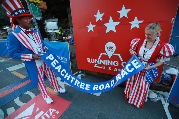 July 4, 2019 Atlanta: Paula & Reg Barnes, dressed as Uncle Sam and Betsy Ross, prepare the finish line tape for the AJC Peachtree Road Race on Thursday, July 4, 2019, in Atlanta. The couple have manned the finish line for more than 30 years.  Curtis Compton/ccompton@ajc.com