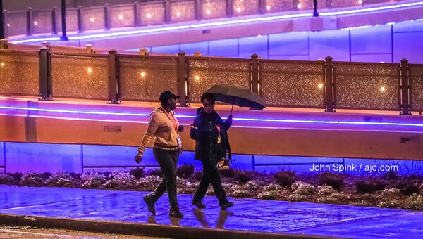 Rain falls on Cynthia Hill Crawley (left) and Vanessa Hall on Tuesday morning as they walk on the pedestrian bridge over Northside Drive near Mercedes-Benz Stadium. JOHN SPINK / JSPINK@AJC.COM