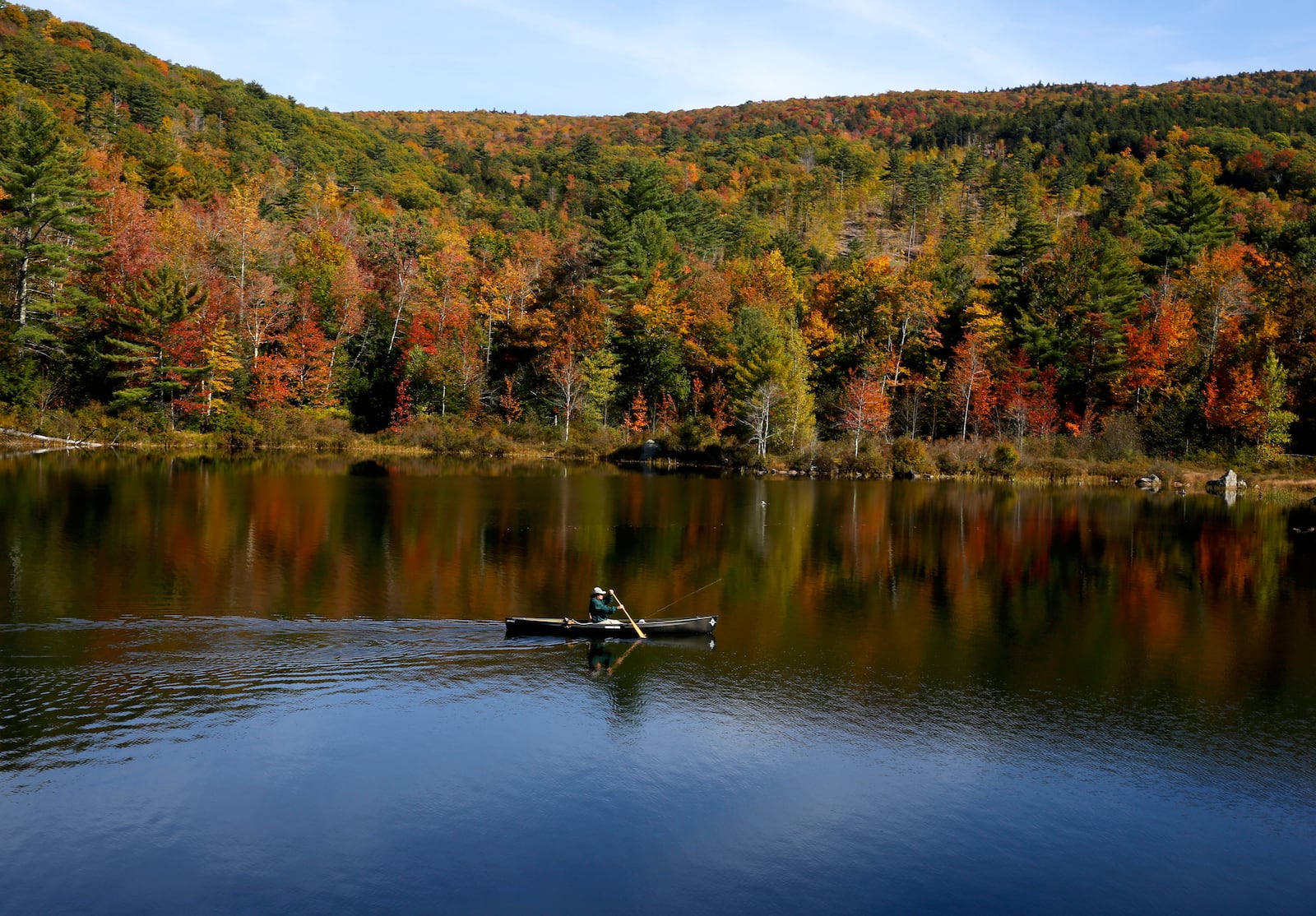 A fly fisherman paddles on a pond as fall foliage begins to show color in Campton, N.H., Sunday, Oct. 6, 2024. (AP Photo/Caleb Jones)