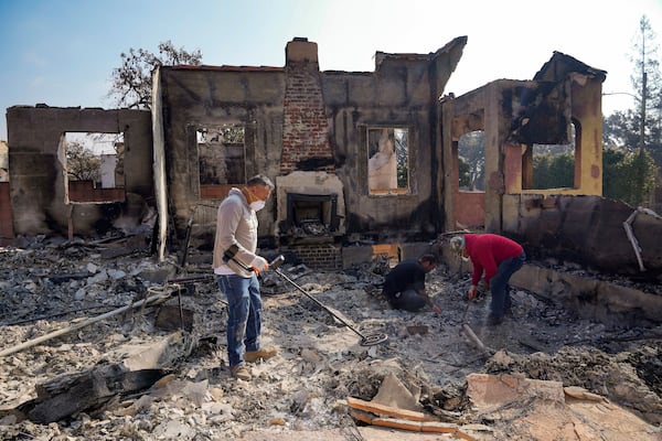 Homeowner David Marquez, left, holds a metal detector as his father, Juan Pablo Alvarado, right, and a friend look for the remains of gold jewelry and other silver items inside the walls of their multi-generational home in the aftermath of the Eaton Fire, Sunday, Jan. 19, 2025, in Altadena, Calif. (AP Photo/Damian Dovarganes)