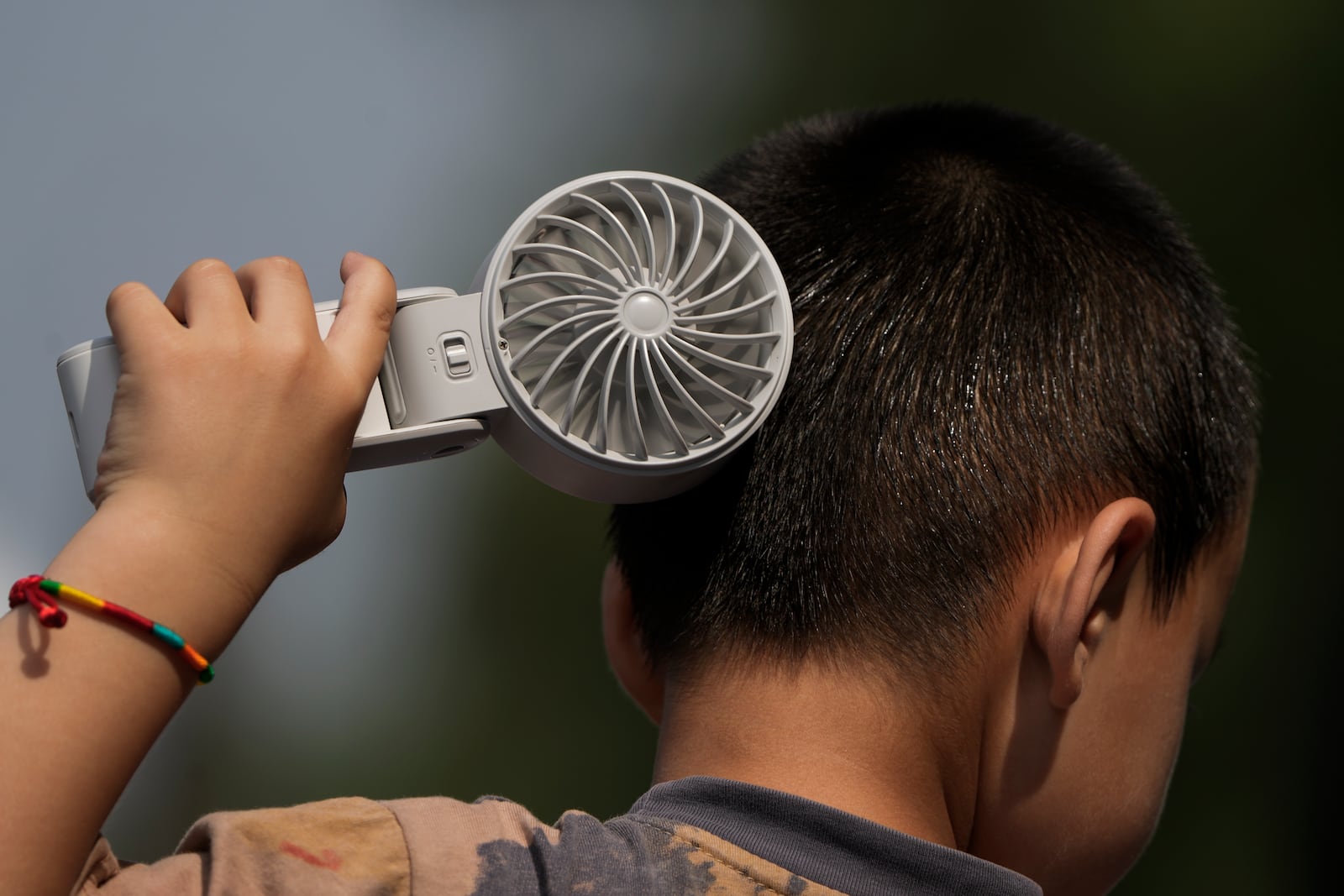 FILE - A boy cools himself with an electric fan on a sweltering day at a park in Tongzhou, on the outskirts of Beijing, Monday, June 10, 2024. (AP Photo/Andy Wong)