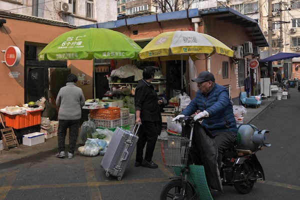 A vendor delivers a gas cylinder passes by residents at a market in Beijing, Sunday, March 9, 2025. (AP Photo/Andy Wong)