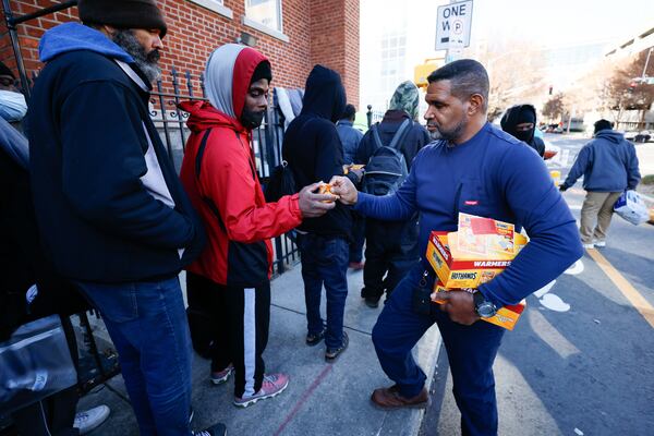 Outreach Supervisor Troy Stephens at the Shrine of the Immaculate Conception passes hand warmers to people waiting in line as they prepare to open their doors for the morning sandwich and snack ministry program. The church serves 200-300 sandwiches, water, and coffee for those in need each weekday.
Miguel Martinez /miguel.martinezjimenez@ajc.com