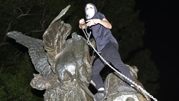 After marching from Woodruff Park to Piedmont Park during a anti white nationalism memorial and march in response to violence in Virginia, a protester climbs a Confederate monument with a chain in an attempt to topple it on Sunday, Aug. 13, 2017, in Atlanta. The peace monument at the 14th Street entrance depicts a angel of peace stilling the hand of a Confederate soldier about to fire his rifle.  (Curtis Compton/Atlanta Journal-Constitution)