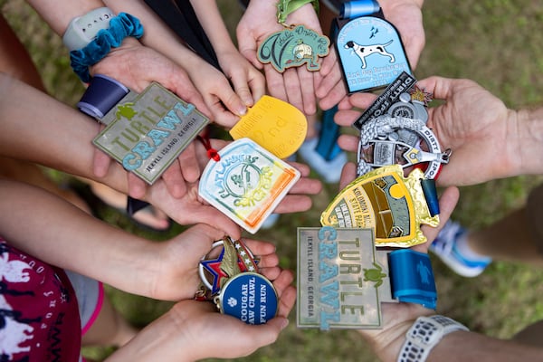 Members of the Coleman family pose with medals from races at their home in Decatur on Thursday, May 23, 2024.  (Arvin Temkar / AJC)