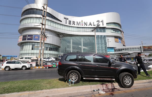 Thai rescue teams walk by a shooting victim’s vehicle outside the Terminal 21 Korat mall.