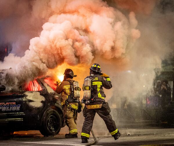 Atlanta firefighters extinguish a police car that was set afire during a Forest Defenders protest in Atlanta Saturday, Jan 21, 2023. The Atlanta Police department said Several arrests had been made. (Steve Schaefer/steve.schaefer@ajc.com)