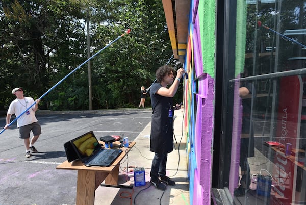 Roberto Hernández works on a mural with volunteers Aaron Whitmoyer (left) and Enna Garkusha (background) outside Atlanta Package store on Buford Hwy on Friday, September 15, 2017. Roberto Hernández is a painter working on a mural as part of the Living Walls project along Buford Highway. He is also a DACA recipient. HYOSUB SHIN / HSHIN@AJC.COM