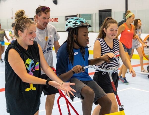 Volunteers Heather Genzale, Corey Fogle and Morgan Laningham (far right) helped special needs camper, Ezekiel, learn how to ride a two-wheel bike without adaptations during the iCan Bike Alpharetta camp at The Cooler in Alpharetta. PHIL SKINNER FOR THE ATLANTA JOURNAL-CONSTITUTION.