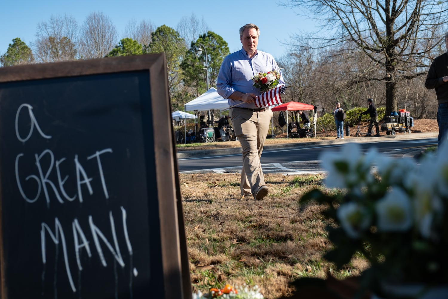 Donovan Head, of Woodstock, brings a flag and flowers to a makeshift memorial to former President Jimmy Carter at the Carter Center in Atlanta on Monday, Dec. 30, 2024. Head had met Carter a few times and said he had a huge impact on him.  Ben Gray for the Atlanta Journal-Constitution