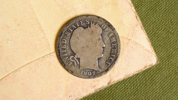 A 1907 Barber Dime on an old and faded yellow envelope and a green textured antique book.