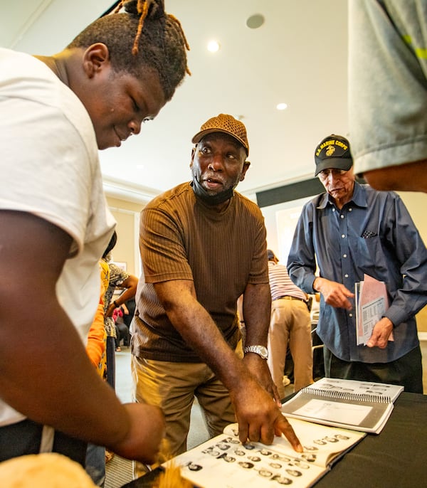 Trenton Kennemore, left, takes a look at his grandfather’s Bailey-Johnson High School photo.  His grandfather Almond Martin, center, and James Emerson were on the 1964-65 basketball team and were presented with their State Championship rings on Monday during the Alpharetta City Council meeting.  (Jenni Girtman for The Atlanta Journal-Constitution)