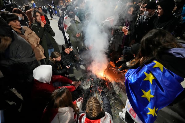 Demonstrators warm themselves by the fire during a rally outside the parliament against the government's decision to suspend negotiations on joining the European Union in Tbilisi, Georgia, on Wednesday, Dec. 4, 2024. (AP Photo/Pavel Bednyakov)