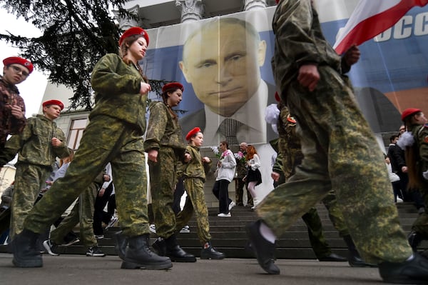 FILE - Youths mark the ninth anniversary of the annexation of Crimea from Ukraine with a banner reading, "Russia doesn't start wars, it ends them," next to an image of Russian President Vladimir Putin in Yalta, Crimea, on March 17, 2023. (AP Photo, File)