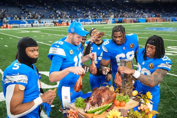 Detroit Lions running back David Montgomery (5) from left, quarterback Jared Goff (16), wide receiver Amon-Ra St. Brown (14), linebacker Al-Quadin Muhammad (69), and running back Jahmyr Gibbs (26) celebrate with turkey after beating the Chicago Bears 23-20 in an NFL football game in Detroit, Thursday, Nov. 28, 2024. (AP Photo/Carlos Osorio)