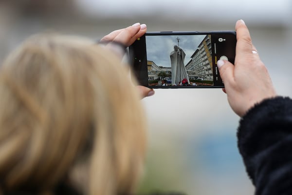 A woman takes a photo of a statue of Pope John Paul II in front of the Agostino Gemelli Polyclinic, in Rome, where Pope Francis has been hospitalized since Friday, Feb. 14, Wednesday, Feb. 26, 2025. (AP Photo/Andrew Medichini)