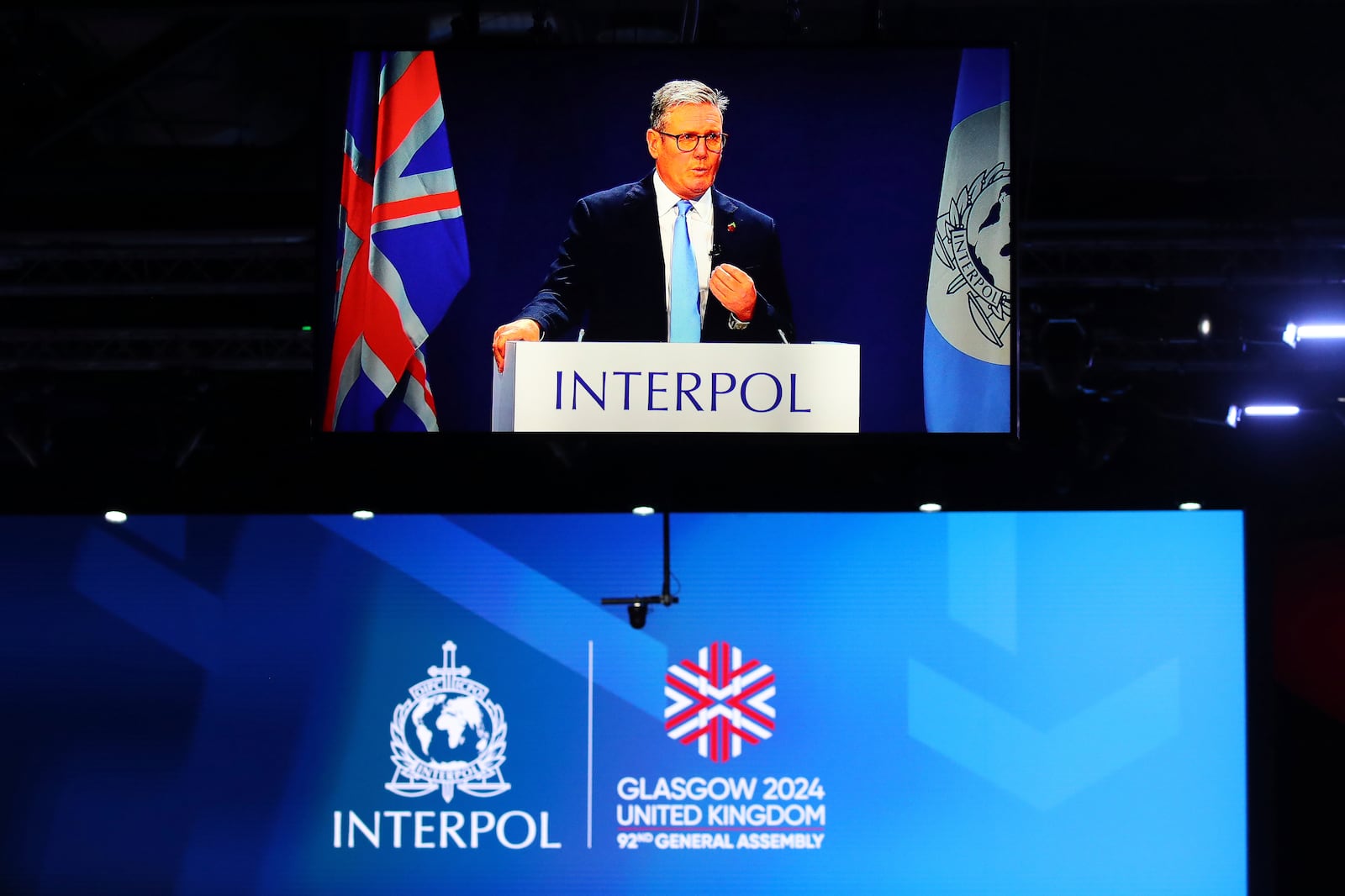 Britain's Prime Minister Keir Starmer, seen on a large video screen, speaking at the opening ceremony for the Interpol General Assembly in Glasgow, Scotland Monday, Nov. 4, 2024. (AP Photo/Scott Heppell)