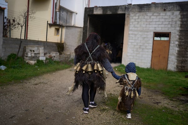 Vasiliki Pergada and her 4-year-old daughter Panagiota, dressed in animal skins and heavy bronze bells, join revelers gathering to take part in carnival celebrations in Distomo, a village in central Greece, on Monday, March 3, 2025. (AP Photo/Petros Giannakouris)