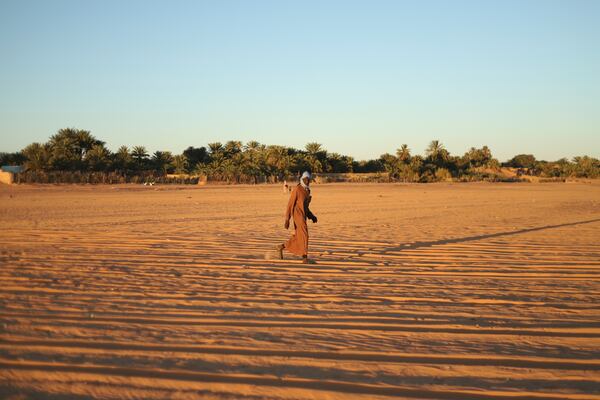 A man walks through sand with palm trees in the distance in Chinguetti, Mauritania on Feb. 3, 2025. (AP Photo/Khaled Moulay)