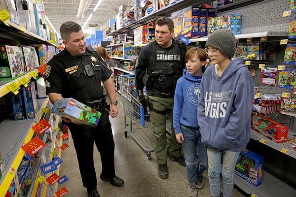 Abel Stevens, 11, center, and his sister Gabriella Bailey, 14, right, of Canton, shop for toys with Sergeant Cody Jones, left, and Deputy Joe Sullivan at Walmart, Tuesday, December 13, 2022, in Canton, Ga. The children were shopping with the Cherokee County Deputies during their annual ‘Shot with a cop’ event to buy toys for underprivileged children. (Jason Getz / Jason.Getz@ajc.com)