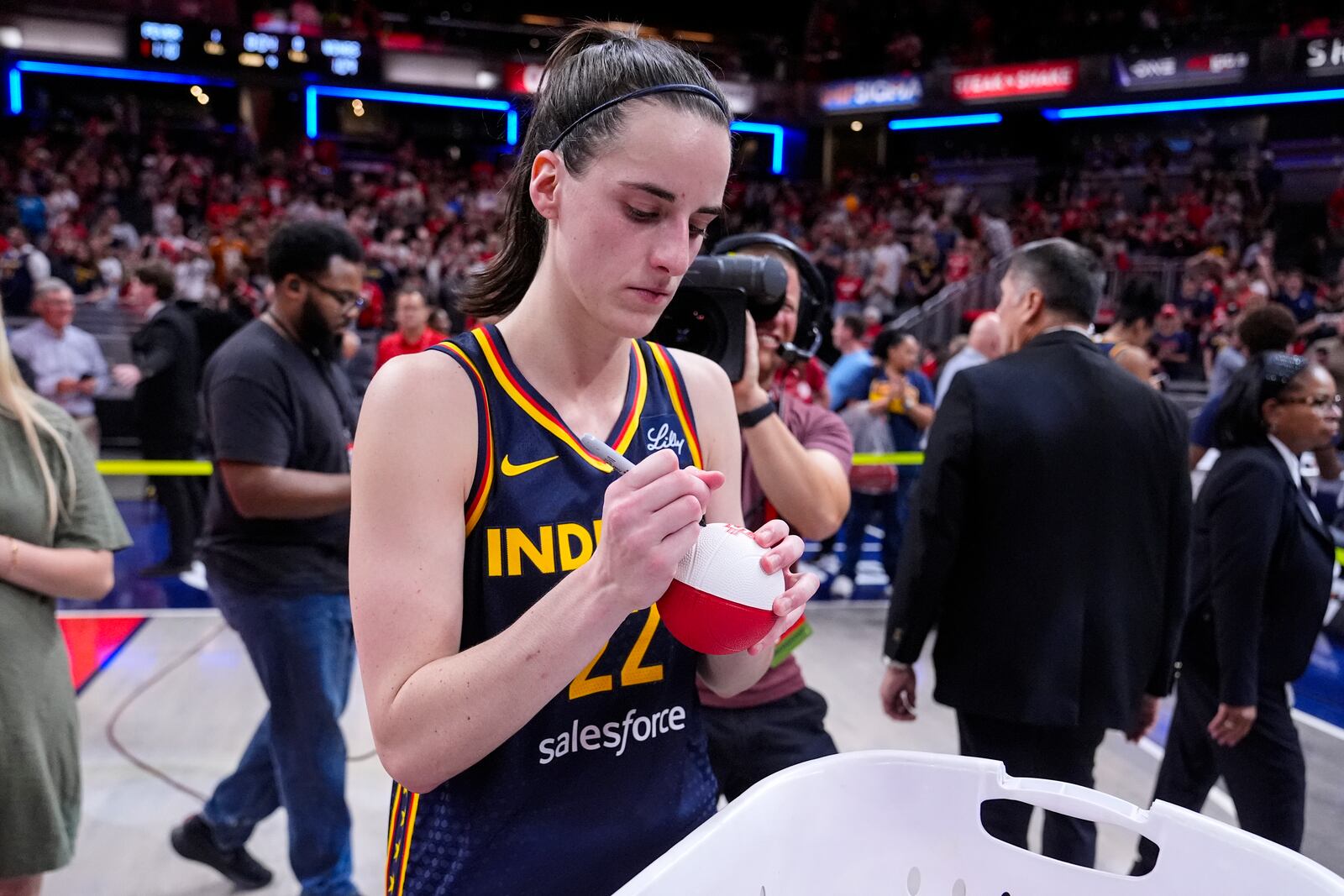 Indiana Fever guard Caitlin Clark (22) signs mini basketballs for fans following in a WNBA basketball game against the Dallas Wings in Indianapolis, Sunday, Sept. 15, 2024. (AP Photo/Michael Conroy)